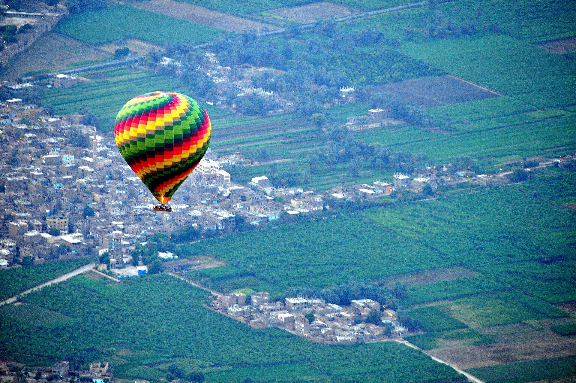 Colorful hot air balloon floating above green fields near Luxor